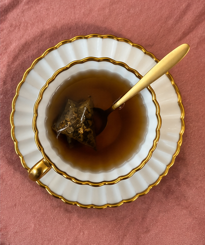 An overhead view of a cup of botanical ritual tea with a gold spoon on a rose cloth